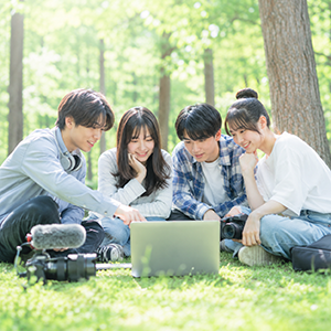 緑の中でパソコンを囲んで動画制作を学ぶ生徒たち